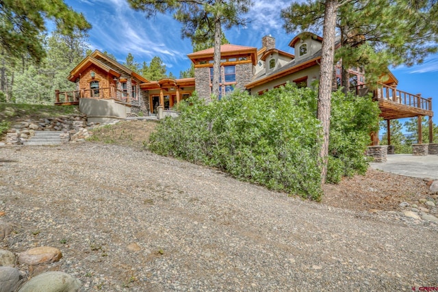 exterior space featuring a chimney, a patio area, a deck, and stone siding