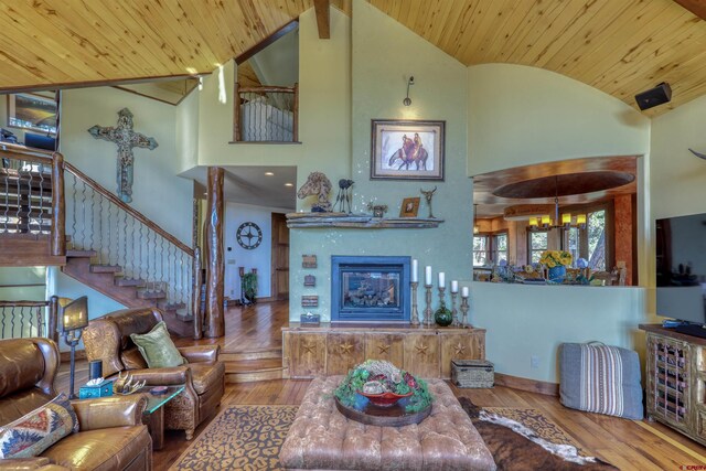 living room featuring hardwood / wood-style flooring, wooden ceiling, high vaulted ceiling, a glass covered fireplace, and stairs
