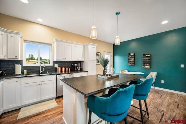 kitchen featuring stainless steel dishwasher, decorative backsplash, dark countertops, a center island, and a sink