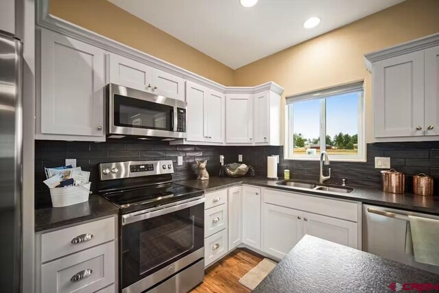 kitchen with decorative backsplash, dark countertops, a sink, light wood finished floors, and stainless steel appliances
