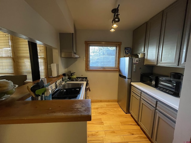 kitchen featuring a sink, butcher block countertops, light wood-style flooring, freestanding refrigerator, and a toaster