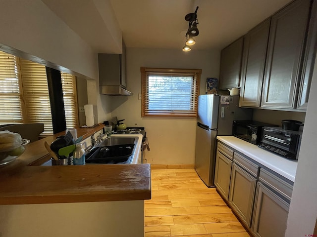 kitchen with freestanding refrigerator, a toaster, light wood-type flooring, a sink, and exhaust hood
