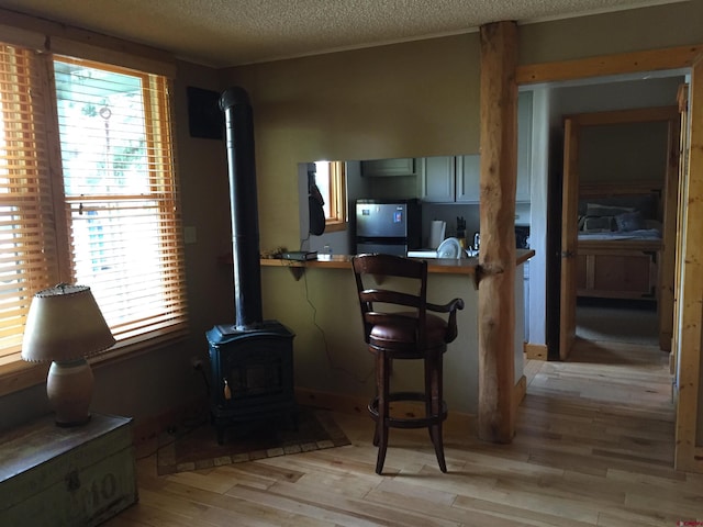interior space featuring a wood stove, freestanding refrigerator, a breakfast bar area, light wood-type flooring, and a textured ceiling