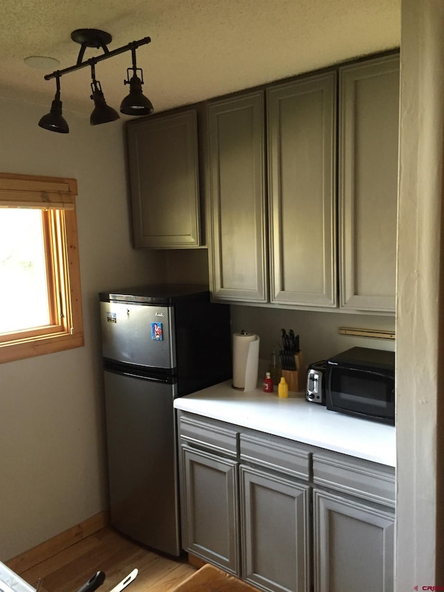 kitchen featuring freestanding refrigerator, black microwave, light wood-type flooring, and light countertops