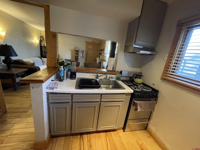 kitchen featuring range hood, a sink, light wood finished floors, open floor plan, and range with gas stovetop