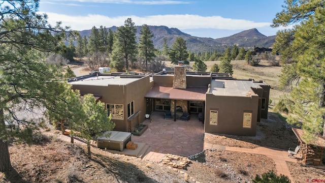 rear view of house with a patio, a mountain view, stucco siding, and a chimney