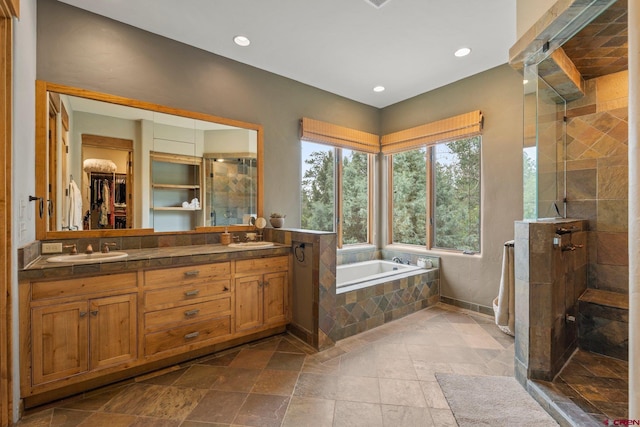 full bath with a garden tub, stone tile floors, double vanity, a sink, and a stall shower