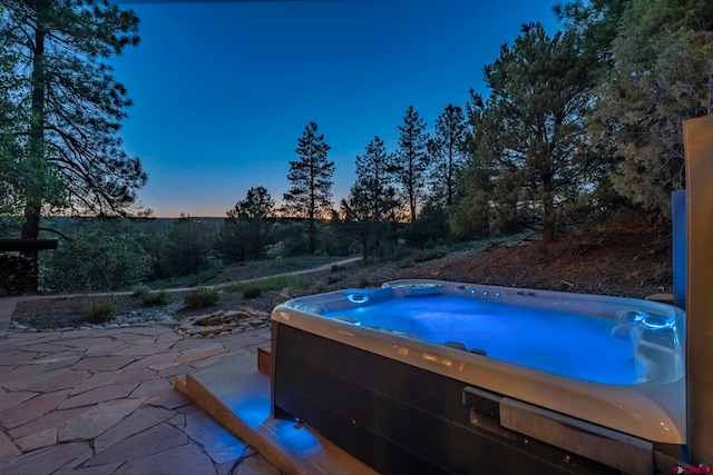 pool at dusk with a hot tub and a patio area