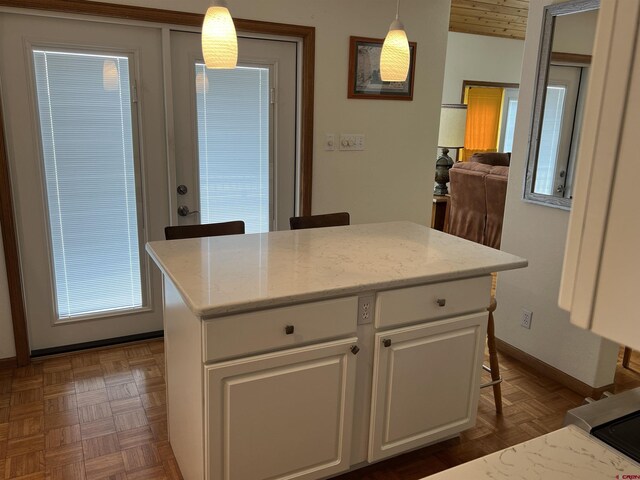 kitchen with light stone counters, a center island, white cabinetry, baseboards, and pendant lighting