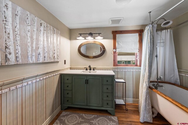 full bath with vanity, a freestanding tub, wood finished floors, and a wainscoted wall