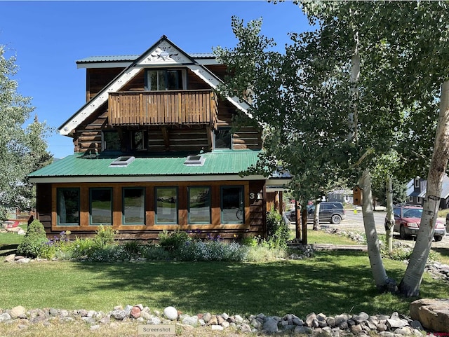 rear view of house featuring a yard, metal roof, and a balcony