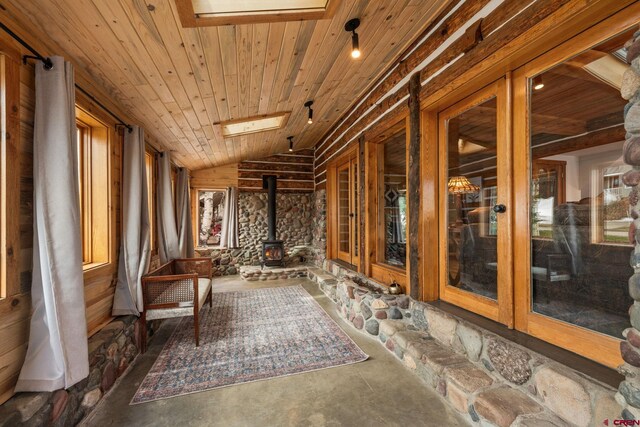 interior space with vaulted ceiling, wooden ceiling, a wood stove, and wood walls