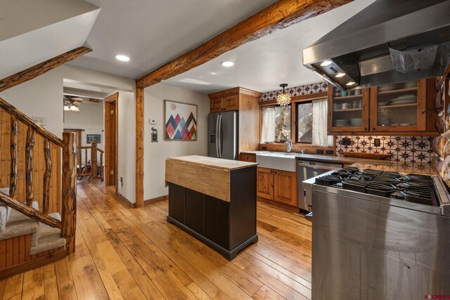 kitchen with stainless steel appliances, light wood finished floors, a sink, and wall chimney exhaust hood