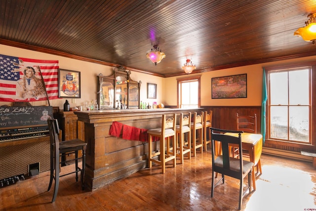 bar with crown molding, a wainscoted wall, hardwood / wood-style flooring, wooden ceiling, and a bar