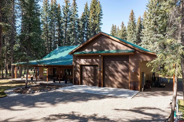 chalet / cabin with a garage, metal roof, and gravel driveway