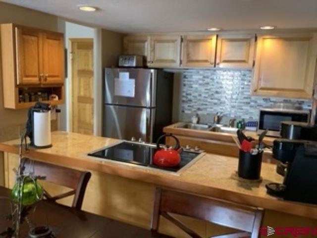 kitchen with decorative backsplash, light countertops, freestanding refrigerator, black electric stovetop, and recessed lighting