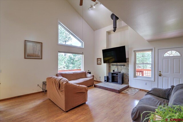 living room featuring track lighting, a wood stove, baseboards, high vaulted ceiling, and light wood-type flooring