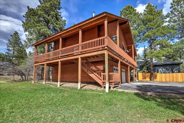 rear view of house featuring driveway, a lawn, a deck, stairway, and fence