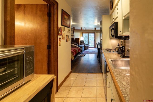 kitchen with black microwave, butcher block countertops, white cabinetry, a sink, and light tile patterned floors