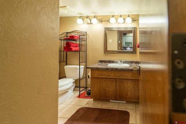 half bathroom featuring tile patterned floors, a textured wall, vanity, and toilet