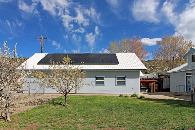 back of property featuring a lawn, a patio, metal roof, and roof mounted solar panels