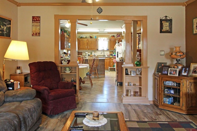 living area featuring ornate columns, crown molding, light wood-style floors, and ceiling fan