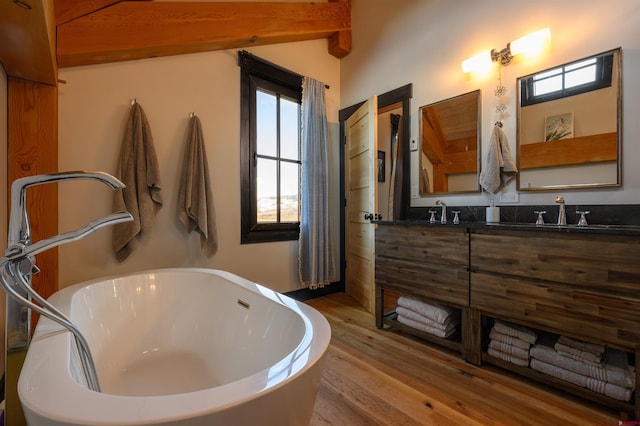 full bath featuring a sink, double vanity, a freestanding tub, wood finished floors, and beamed ceiling
