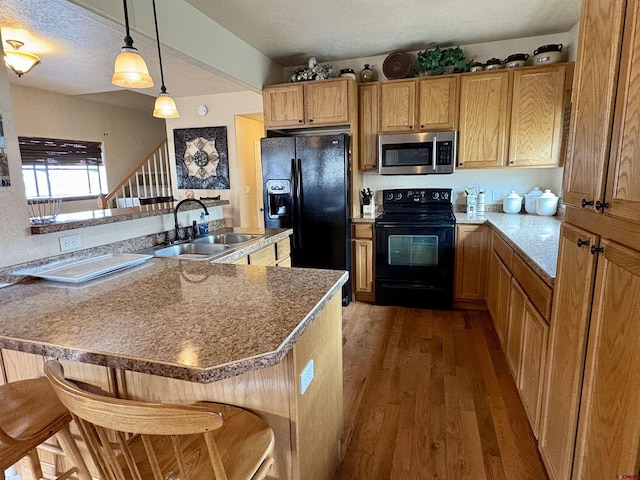 kitchen with hanging light fixtures, a sink, a kitchen breakfast bar, wood finished floors, and black appliances