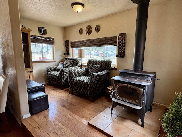 living area with baseboards, a textured ceiling, light wood-style flooring, and a wood stove