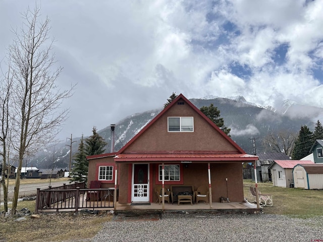 back of property with a storage unit, stucco siding, a deck with mountain view, an outbuilding, and metal roof