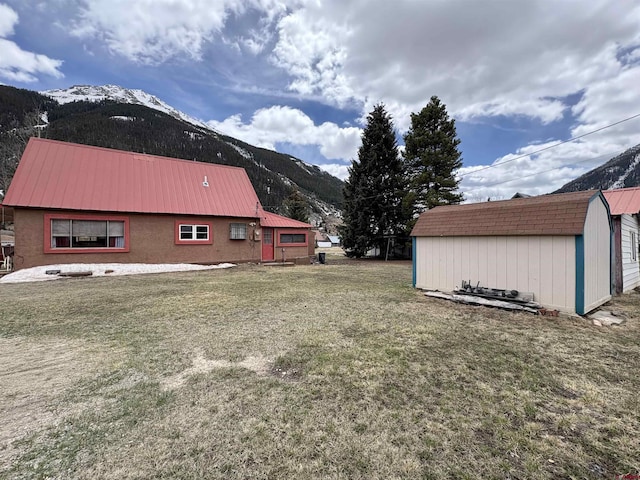 view of property exterior featuring metal roof, a storage shed, a lawn, an outbuilding, and a mountain view