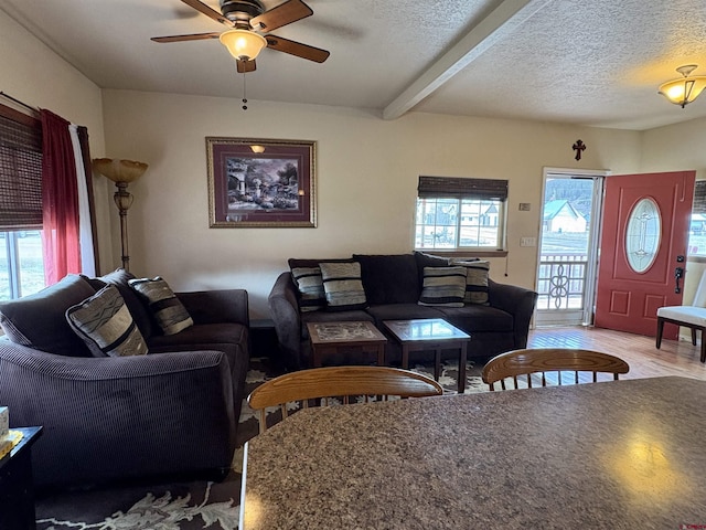 living area featuring a ceiling fan, beamed ceiling, wood finished floors, and a textured ceiling