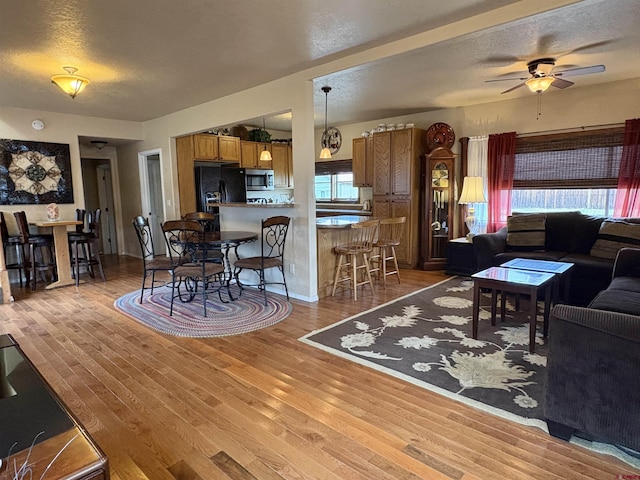 living room with a textured ceiling, light wood finished floors, and ceiling fan