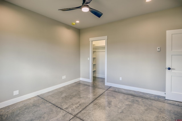 unfurnished bedroom featuring recessed lighting, baseboards, a walk in closet, and finished concrete flooring