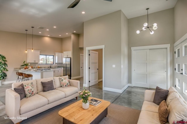 living room featuring an inviting chandelier, concrete floors, recessed lighting, baseboards, and a towering ceiling