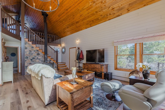 living area featuring stairs, wooden walls, high vaulted ceiling, light wood-type flooring, and a baseboard heating unit