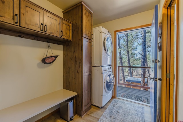 washroom featuring stacked washer / drying machine, light wood finished floors, and cabinet space