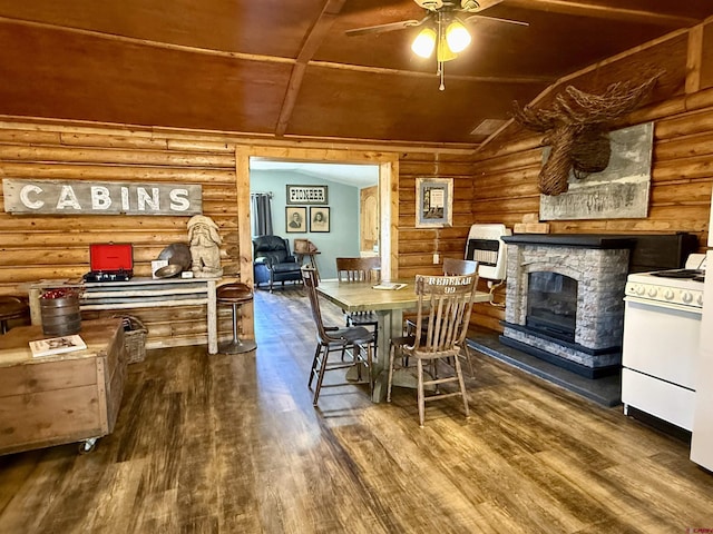 dining space featuring rustic walls, wood finished floors, a stone fireplace, ceiling fan, and vaulted ceiling