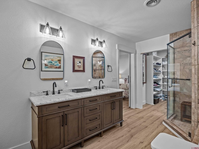 full bath featuring a sink, double vanity, a stall shower, and wood finished floors