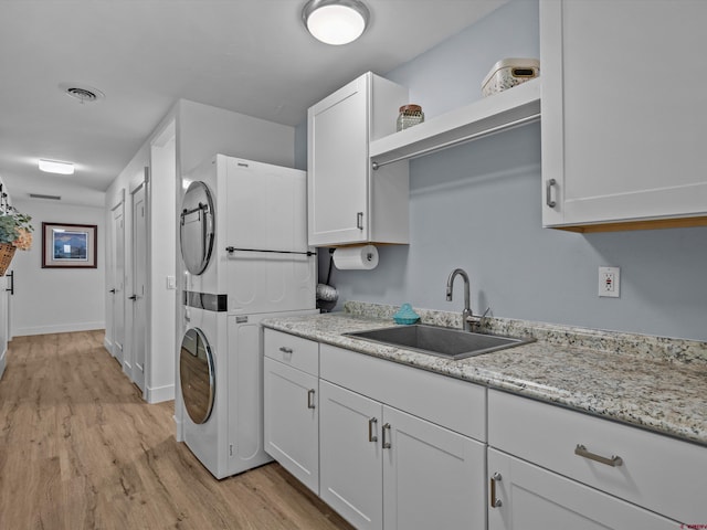 washroom with visible vents, light wood-style floors, baseboards, a sink, and stacked washer / drying machine