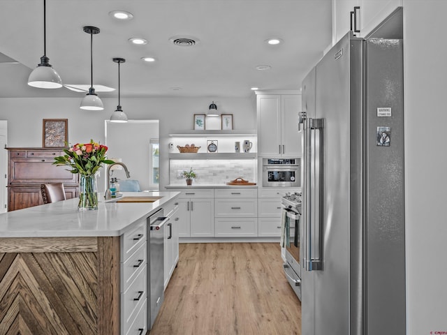 kitchen with a sink, light wood finished floors, appliances with stainless steel finishes, and white cabinetry