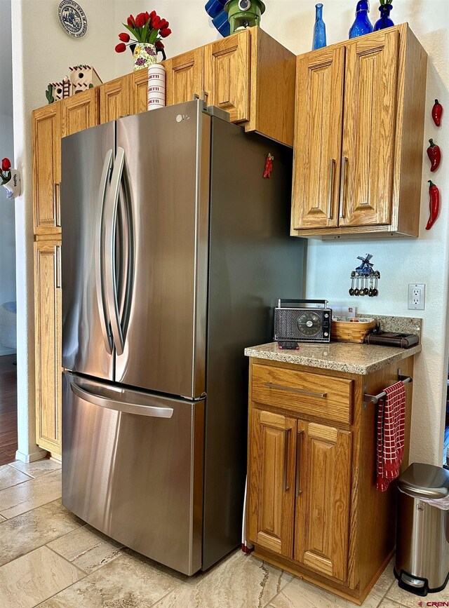 kitchen with freestanding refrigerator, stone finish flooring, brown cabinets, and light stone countertops