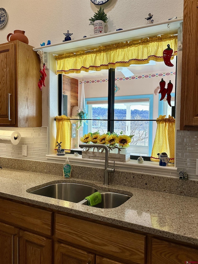 kitchen with light stone counters, a sink, brown cabinetry, and backsplash