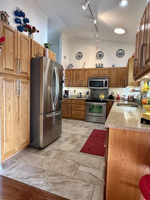 kitchen with appliances with stainless steel finishes, tasteful backsplash, a sink, light stone counters, and track lighting