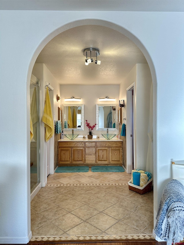 bathroom with double vanity, a textured ceiling, tile patterned flooring, and a stall shower