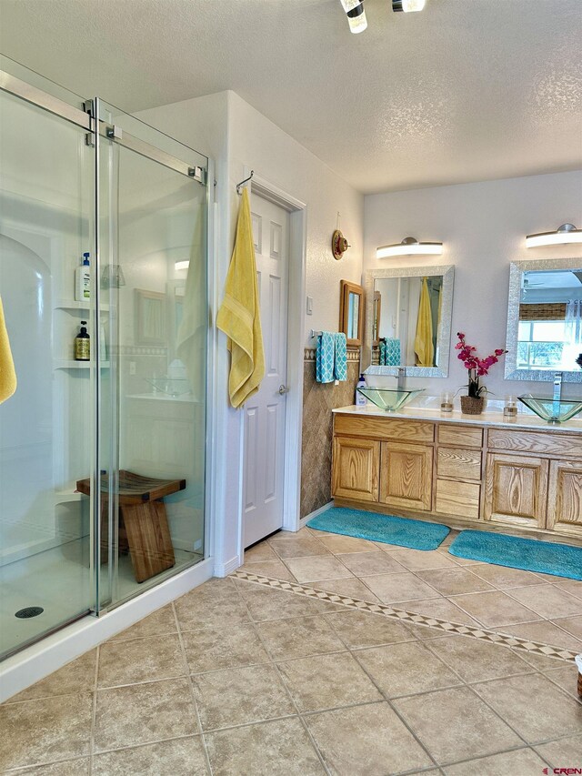 bathroom with double vanity, a shower stall, and a textured ceiling