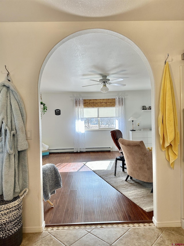 interior space featuring tile patterned flooring, baseboards, a baseboard radiator, a textured ceiling, and arched walkways