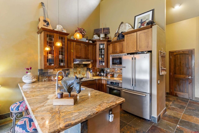kitchen with a towering ceiling, a peninsula, under cabinet range hood, a sink, and stainless steel appliances