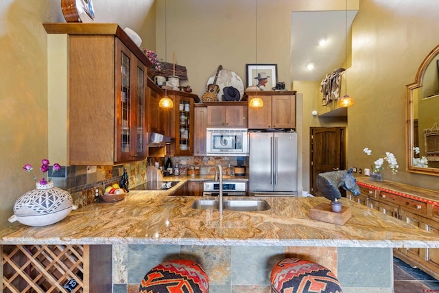 kitchen featuring a peninsula, light stone countertops, a high ceiling, a sink, and stainless steel appliances