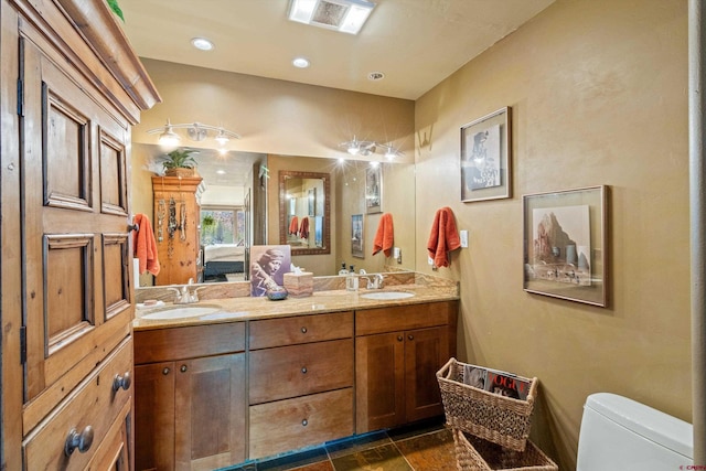 ensuite bathroom featuring double vanity, a sink, visible vents, and toilet